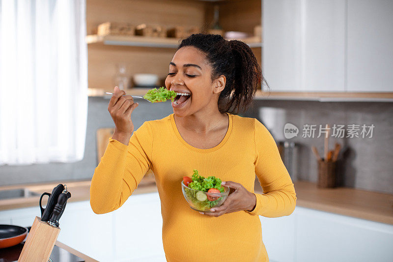 微笑饥饿的年轻怀孕非洲裔美国妇女吃沙拉的有机蔬菜