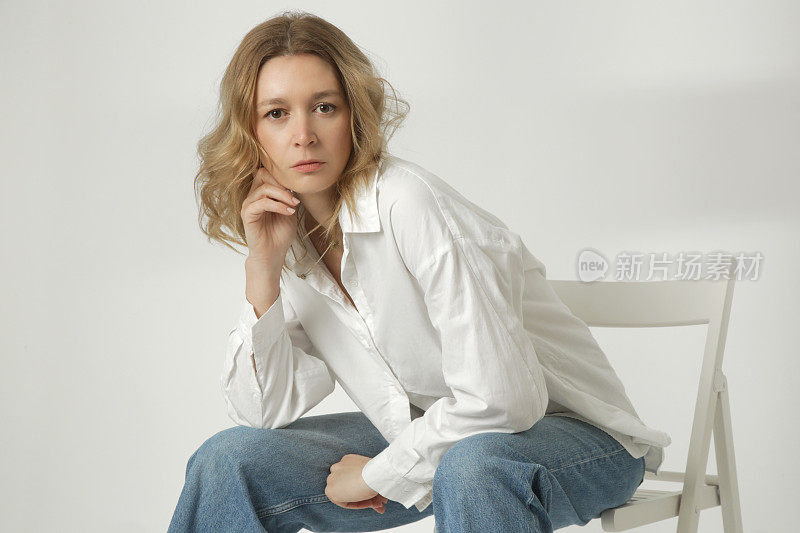 年轻女子的时尚肖像在白色背景上的白色棉布衬衫和蓝色牛仔裤