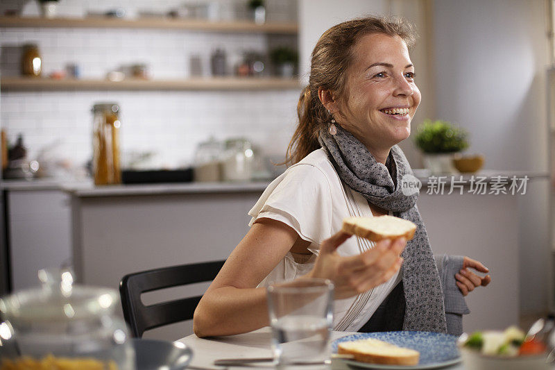 快乐的年轻女人在家里吃三明治。
