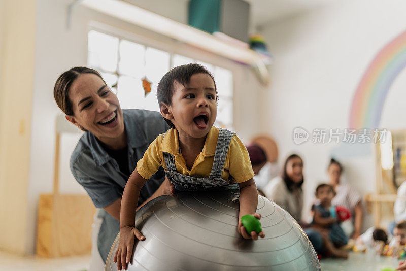 一位中年妇女和她蹒跚学步的男孩在游戏室的健身球上玩耍