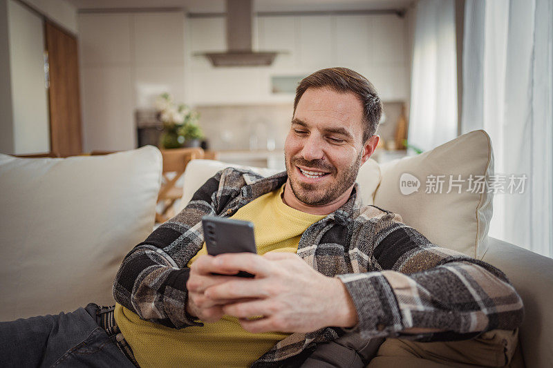 一个成熟的白人男子手里拿着手机，在滚动着收到的信息时，脸上露出喜悦的表情。