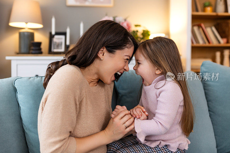 幸福美满的家庭。母亲和女儿玩耍，亲吻和拥抱。可爱的小女孩在家里和妈妈打招呼。母亲节的概念