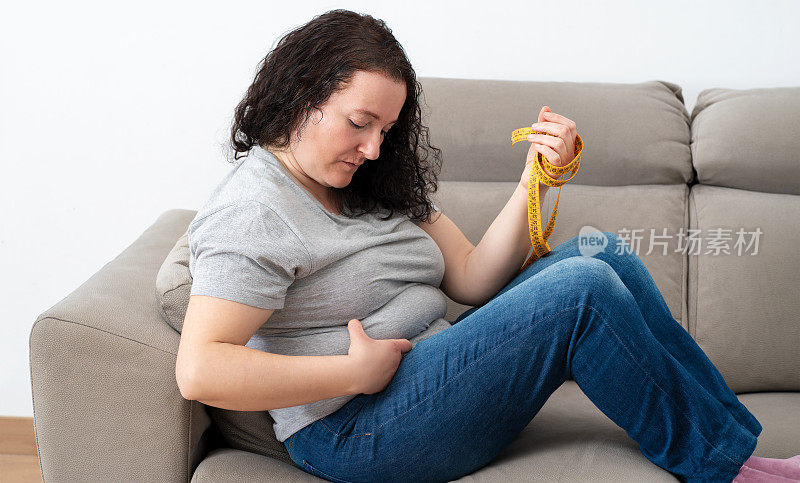 肥胖的女人坐在沙发上检查她的脂肪