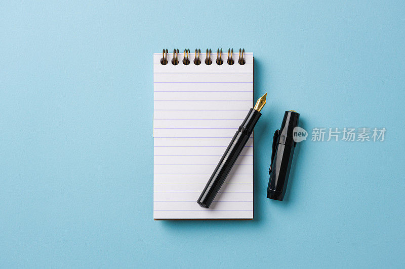 笔记本和钢笔在蓝色背景上的顶视图