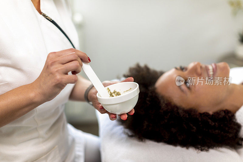 美容专家在一个水疗中心给一个女人的脸上放草药