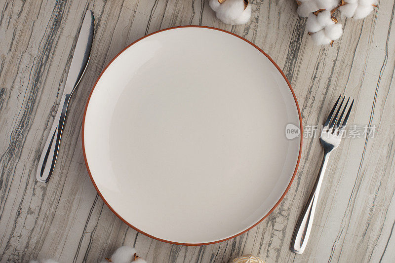 用刀叉清空白色盘子，在石板背景上放上棉花树枝，为你的菜单或食谱留出复制空间。菜单卡餐厅和餐桌设置。水平的照片。平躺