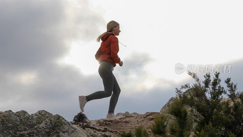 年轻的女子越野跑者在日出时越过山脊