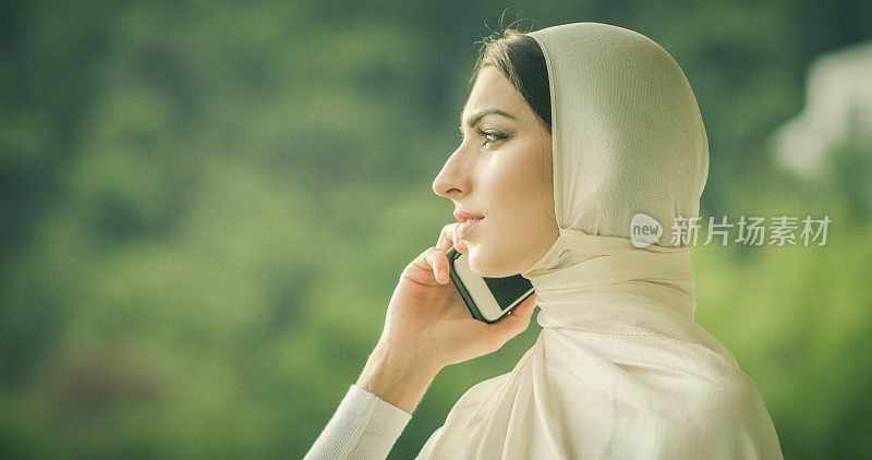 年轻迷人的穆斯林女性在hijab打字电话的特写肖像