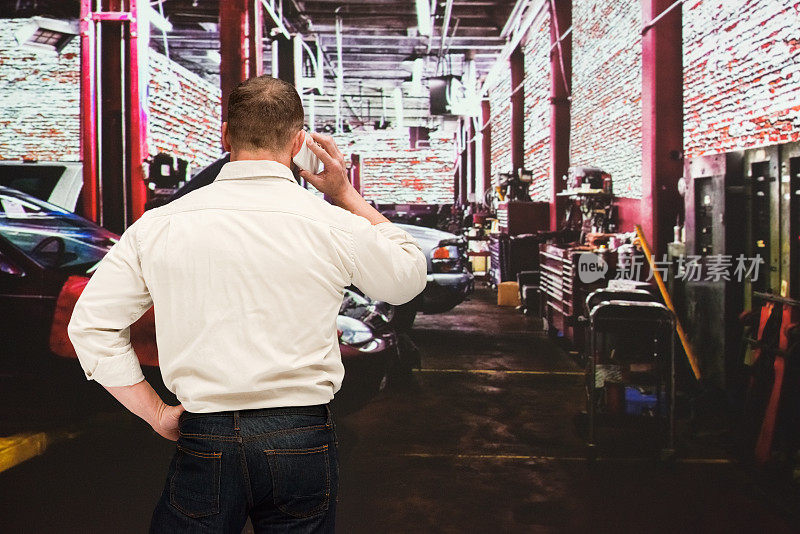 白人年轻男性体力劳动者穿着牛仔裤和使用智能手机在汽车修理店修理