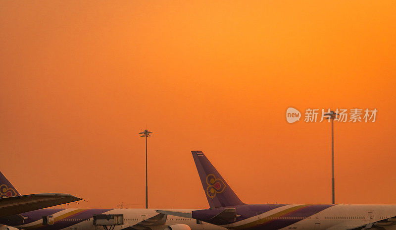 泰国航空公司的航空公司。一架商用飞机停在机场，夕阳下的天空是橙色的。冠状病毒造成全球航空业务危机。航空运输。