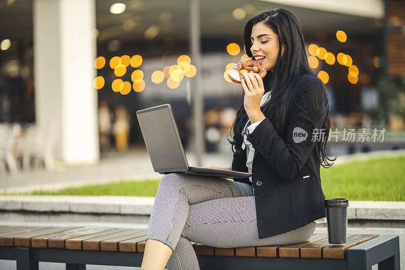 女商人用手提电脑，在公园长椅上吃零食