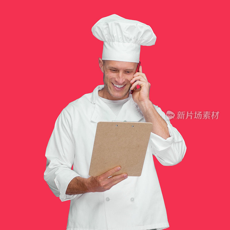 白人年轻男厨师站在有色背景下，穿着裤子，拿着要做的清单，使用手机