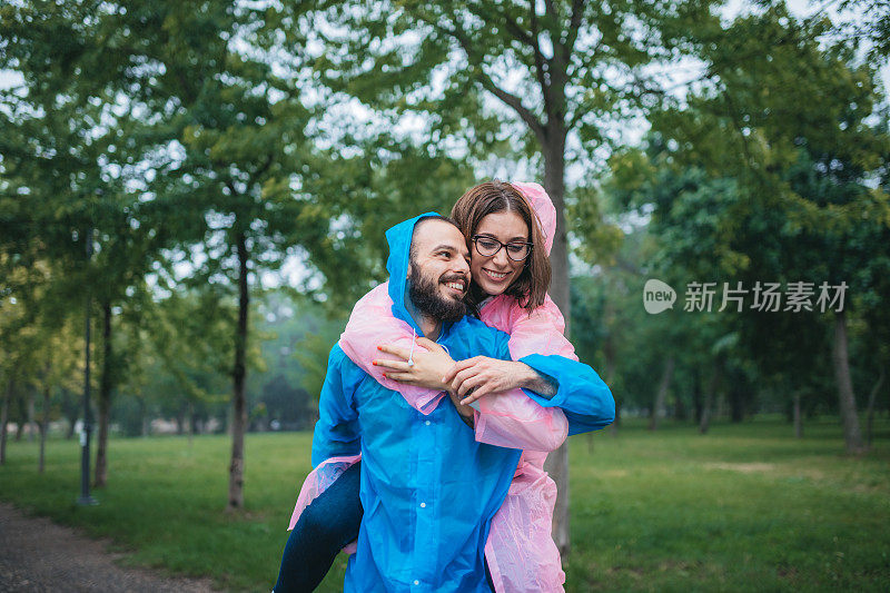 快乐的年轻夫妇在雨中在公园里穿着雨衣