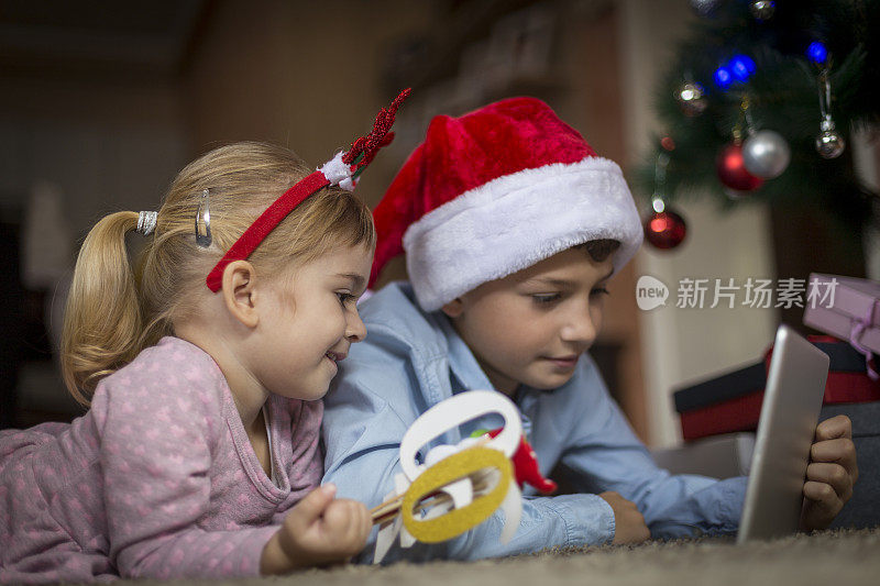 快乐的女孩戴着圣诞发饰看着哥哥手里的数字平板电脑