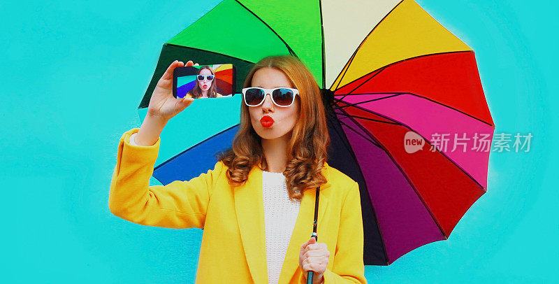 有吸引力的年轻女子的肖像用手机拿着彩色伞在蓝色的背景自拍照片