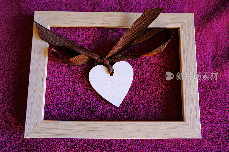白色木制心与丝绸弓横跨木制画框上的紫色纺织品背景特写。副本的空间。爱情概念，圣瓦伦丁节