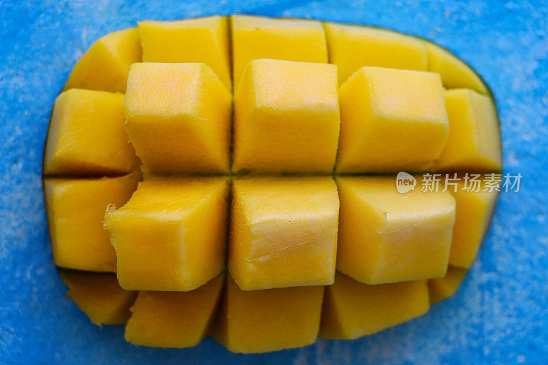特写图片:熟透的桔汁芒果果肉切成两半，切成刺猬方块形状，蓝色背景上切成热带芒果切片，即食，高视野
