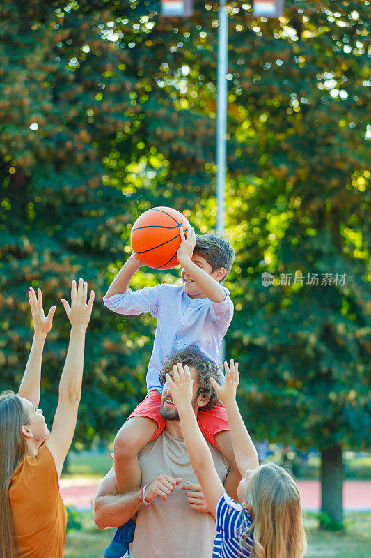 一个快乐的家庭正在操场上享受打篮球。