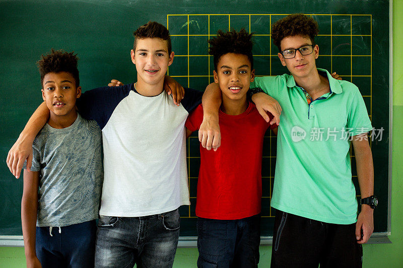 四个男孩站在黑板前，摆姿势照相。