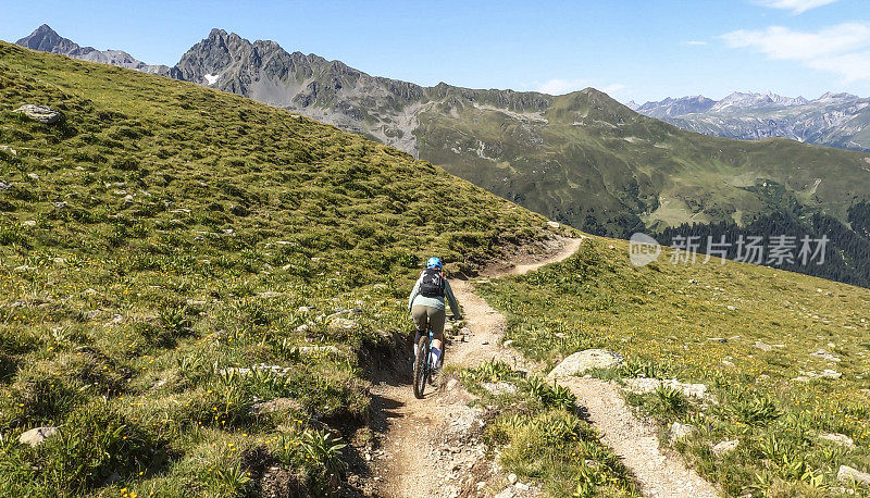 女人沿着阳光明媚的自行车道骑山地车