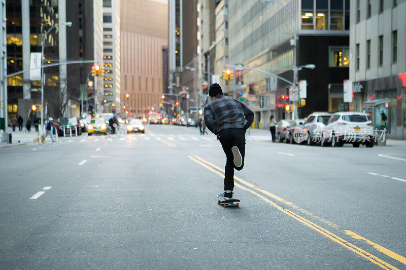 年轻的滑板者的背影沿着城市街道巡航