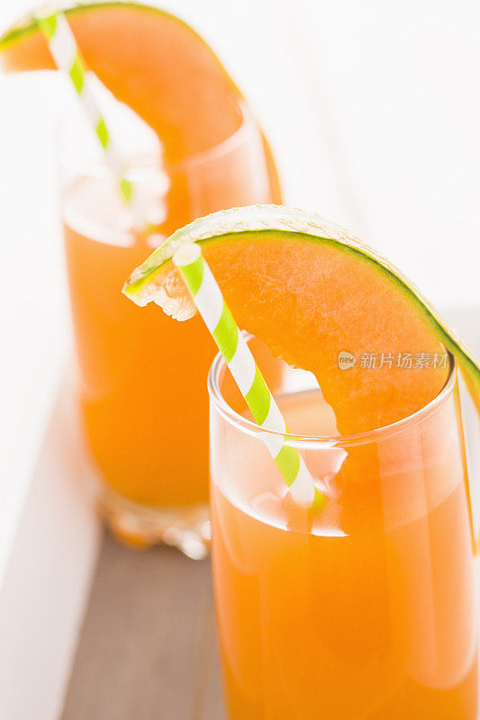 新鲜的甜瓜汁装在玻璃杯中，用吸管饮用