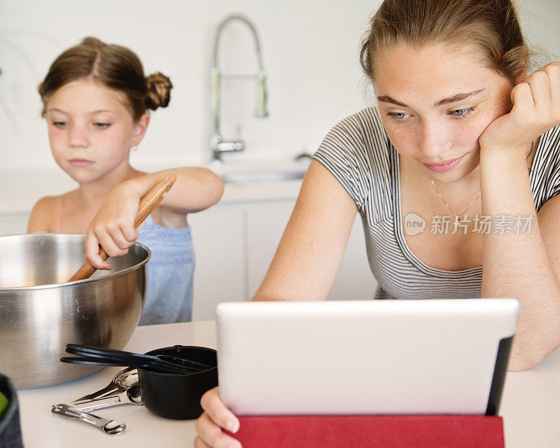 青少年和小女孩在数字平板电脑上遵循食谱。