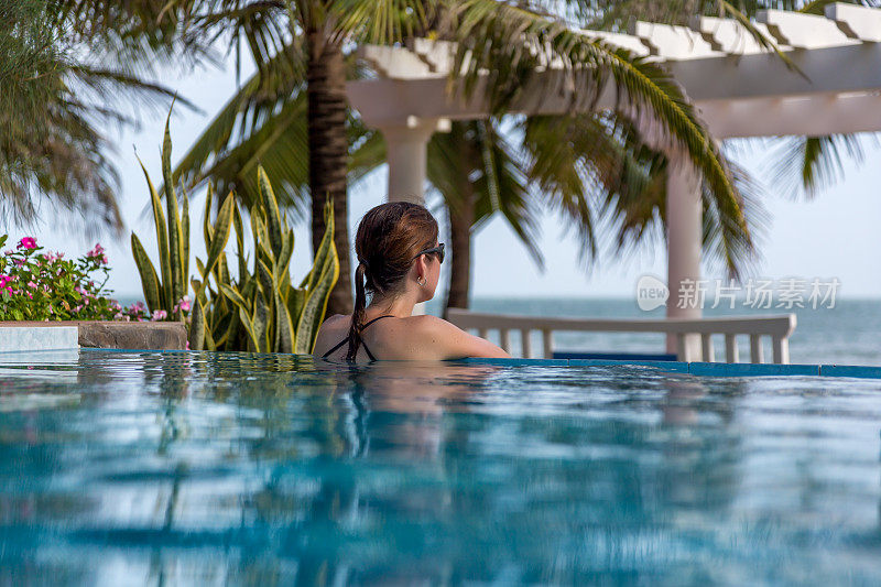 在热带度假村无限泳池内放松的女人