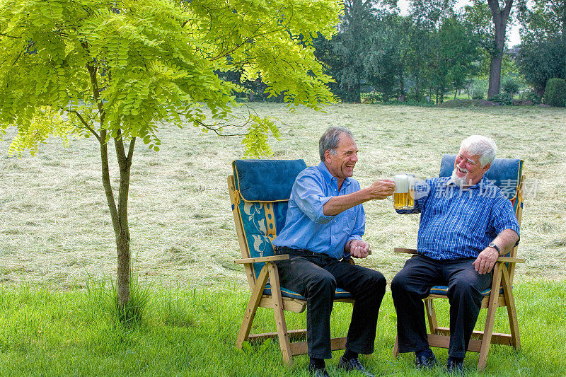 快乐的老人拿着啤酒坐在花园里
