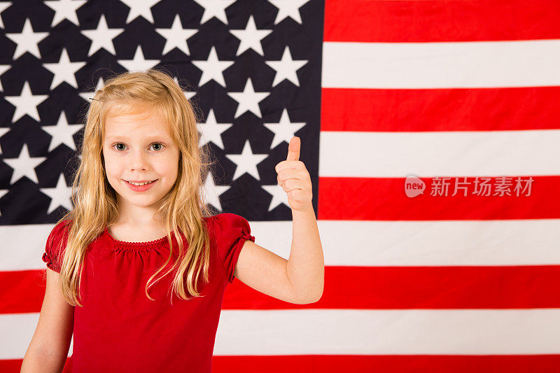 快乐的小女孩在美国国旗上竖起大拇指