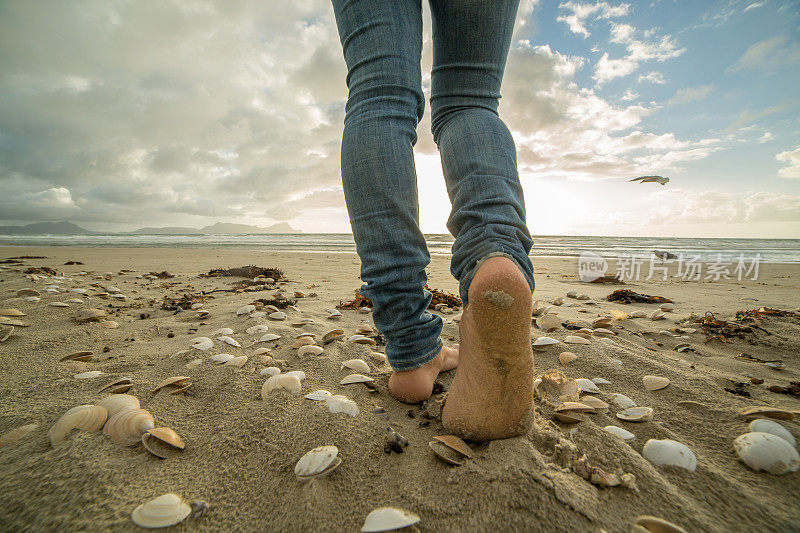 女性的脚在日落时走在海滩上的特写