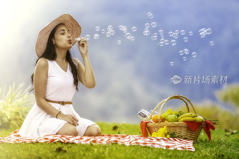 放松的年轻女子吹肥皂泡在草地上公园