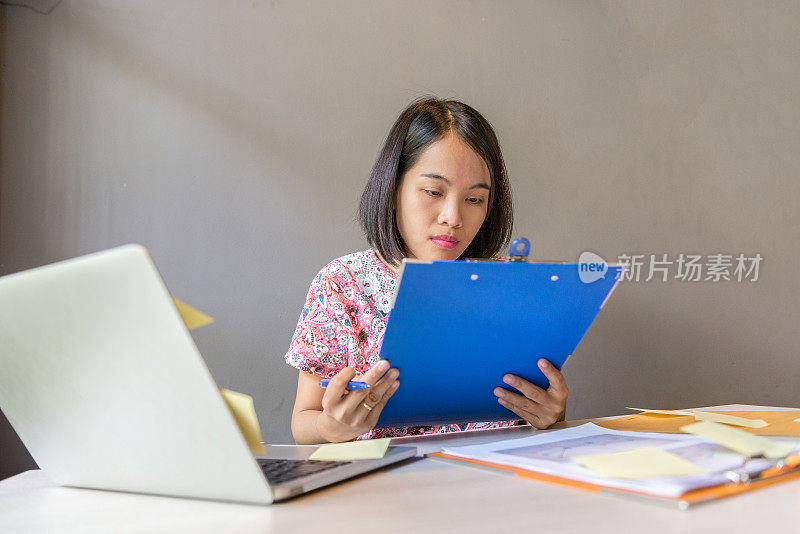 年轻的亚洲女性专注于阅读笔记本电脑旁边的文件
