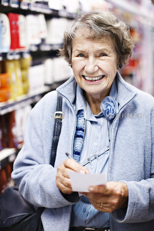 一位面带微笑的老妇人在超市检查她的购物清单