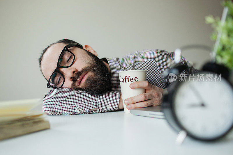 男人睡在办公桌上，上面放着笔记本电脑和咖啡