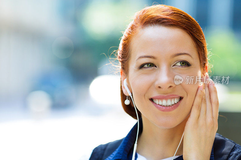 迷人的快乐，微笑的商业女人走在街上听音乐，在户外笑