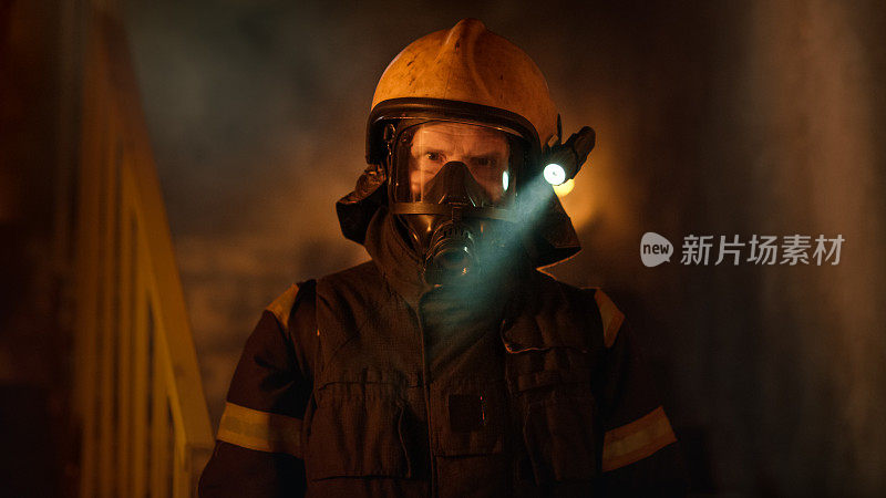 肖像拍摄的一个勇敢的消防员站在一个燃烧的建筑物熊熊大火在他身后。背景中的明火和烟雾。