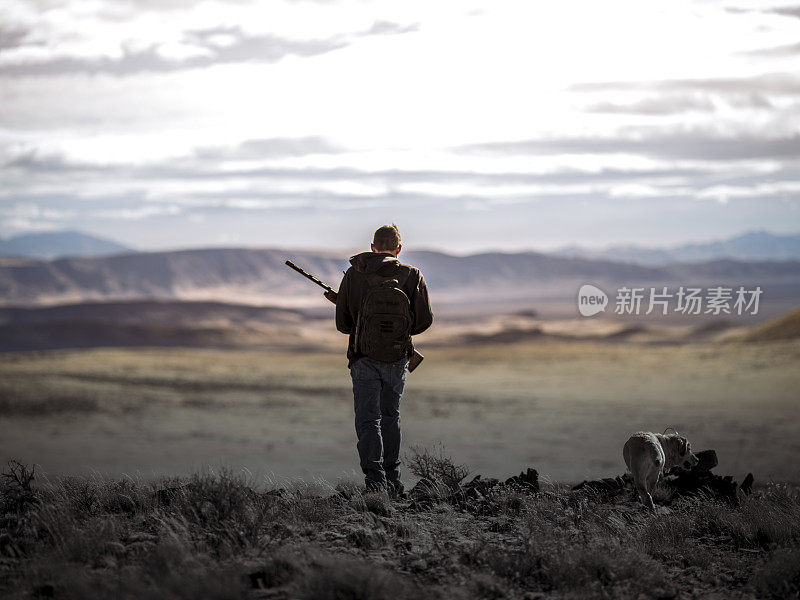 千禧猎人和一只黄色拉布拉多猎犬在崎岖的内华达州沙漠中行走。