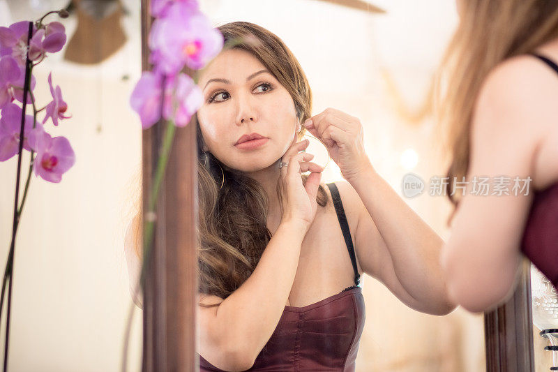 美丽的亚洲女人看着古董镜子，戴着耳环