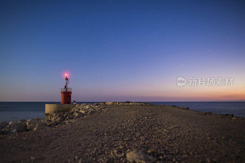 一幅海景，一条宽阔的道路通向一个小灯塔。这张照片摄于意大利萨波迪亚海滩的日落时分
