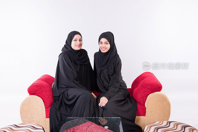 两个阿拉伯妇女坐在家里的沙发椅上聊天