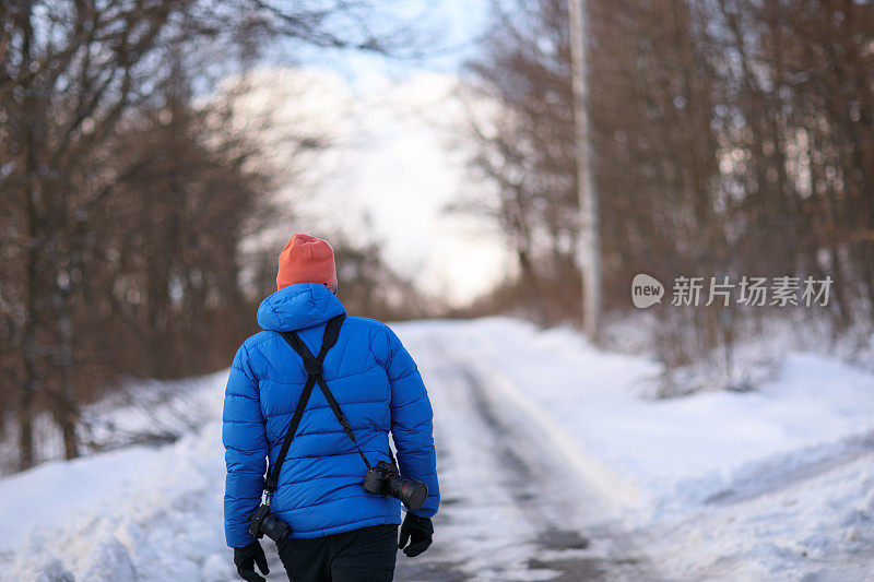 徒步摄影师在白雪覆盖的森林道路上