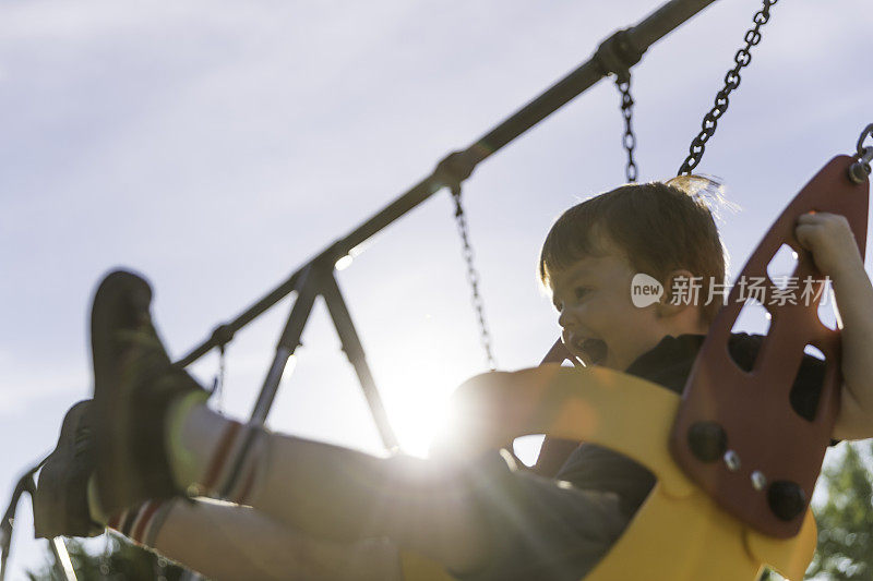 快乐的红发蹒跚学步的男孩坐在操场上的户外秋千