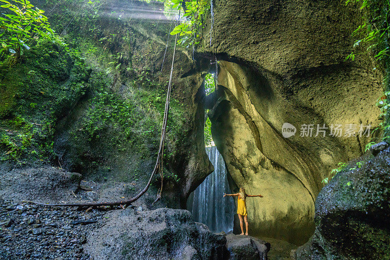 在巴厘岛的热带雨林中，旅行的年轻女子张开双臂拥抱大自然的美丽。人们以自然为旅游理念。