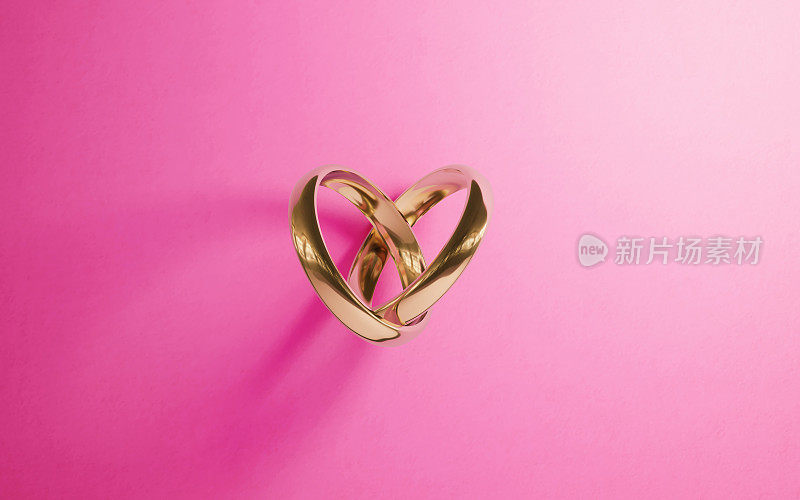 在粉红色背景上形成心形的金结婚戒指