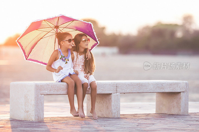 两位年轻的女性朋友坐在日落时分的海滩上