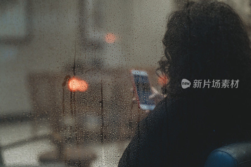 一个下雨天，一个沉思的女人在商店橱窗边用智能手机发短信