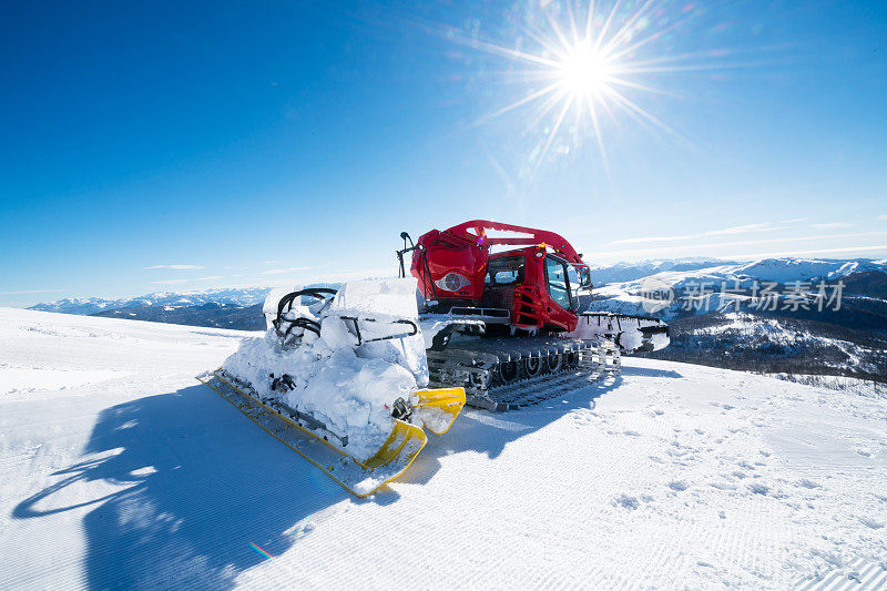 在一个阳光明媚的日子里，在山上清理滑雪道上多余的雪，并给它梳理