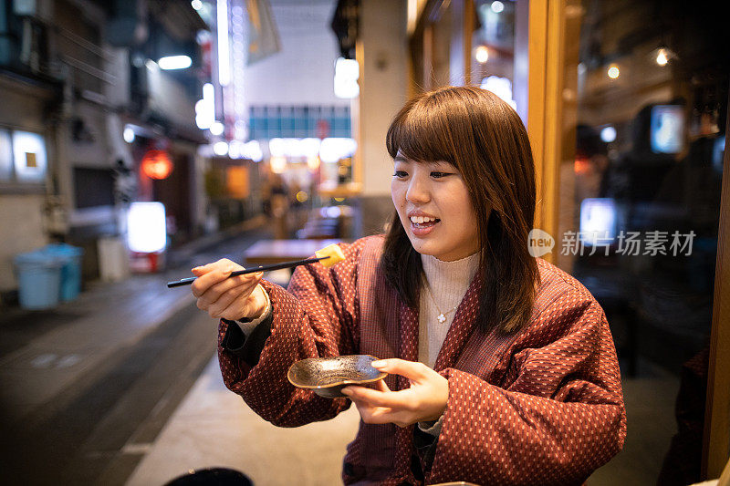在居酒屋户外餐厅吃日本食物的年轻女子