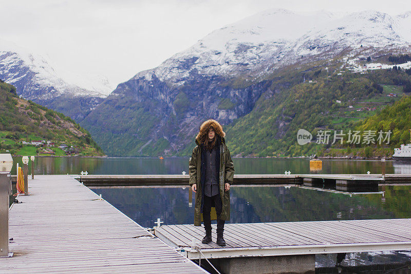 挪威山脉背景下的男子剪影。与峡湾景观。穿着雨衣的游客在盖朗峡湾上。雪在山上。斯堪的那维亚。北自然。Experiental旅行。雨衣
